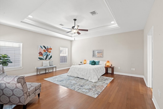 bedroom with hardwood / wood-style floors, ceiling fan, and a tray ceiling