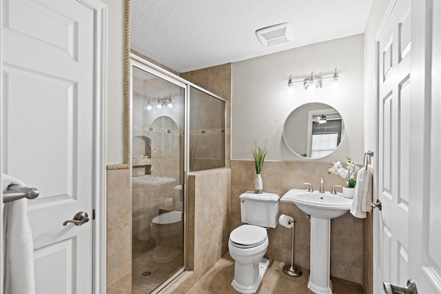 bathroom with tile patterned floors, a textured ceiling, a shower with door, tile walls, and toilet