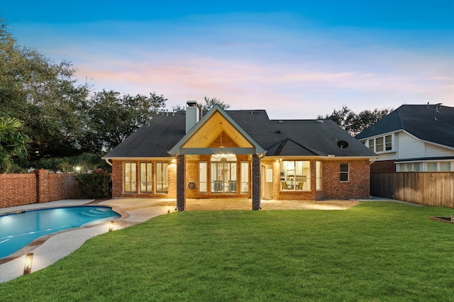 back house at dusk with a fenced in pool and a yard