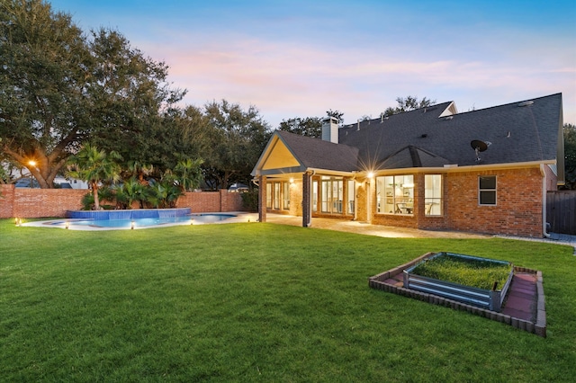 back house at dusk with a yard, a fenced in pool, and pool water feature