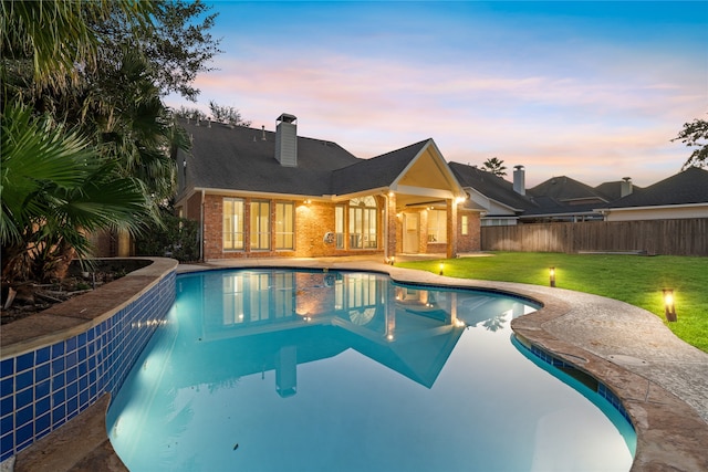 pool at dusk with a yard and a patio