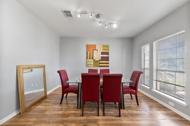 dining area with dark hardwood / wood-style flooring, rail lighting, and plenty of natural light