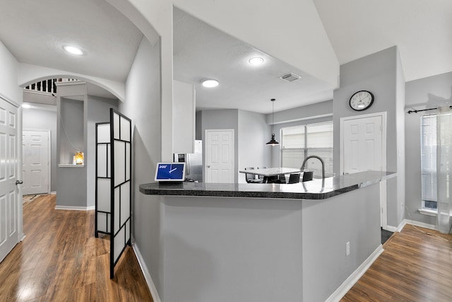 kitchen with kitchen peninsula, hanging light fixtures, white cabinets, and dark wood-type flooring