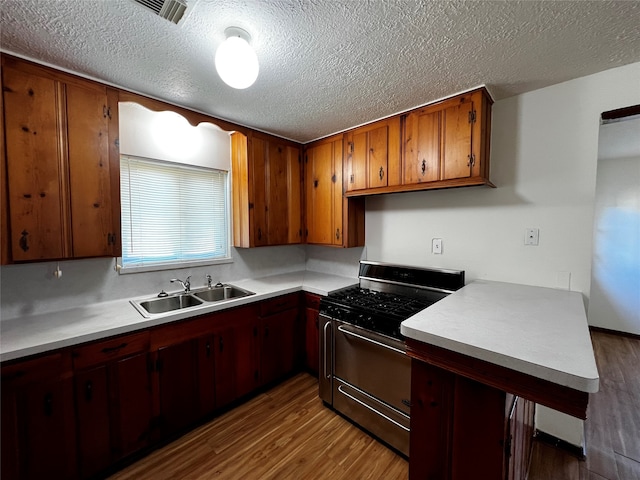 kitchen featuring a textured ceiling, gas range, sink, and dark hardwood / wood-style floors