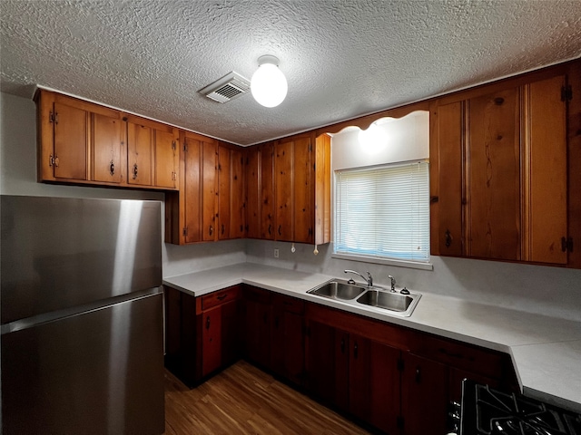 kitchen featuring stainless steel fridge, stove, a textured ceiling, sink, and wood-type flooring