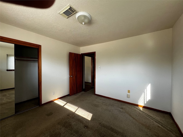 unfurnished bedroom featuring dark carpet, a textured ceiling, and a closet