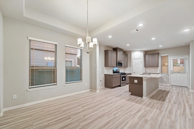 kitchen featuring hanging light fixtures, an island with sink, a chandelier, appliances with stainless steel finishes, and light wood-type flooring