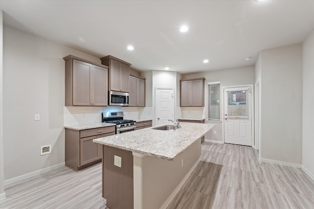 kitchen featuring a center island with sink, sink, light stone countertops, light hardwood / wood-style floors, and stainless steel appliances