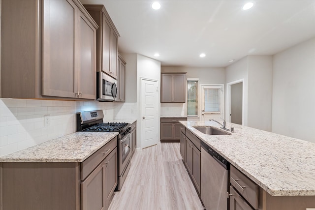 kitchen featuring sink, light stone counters, light hardwood / wood-style floors, a kitchen island with sink, and appliances with stainless steel finishes