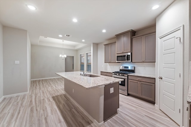 kitchen with a center island with sink, light hardwood / wood-style flooring, light stone counters, stainless steel appliances, and a chandelier