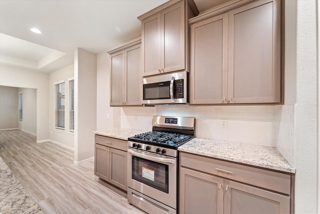 kitchen with decorative backsplash, appliances with stainless steel finishes, light hardwood / wood-style flooring, and light stone counters