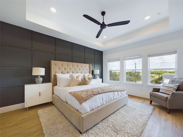 bedroom featuring light wood-type flooring, a raised ceiling, and ceiling fan