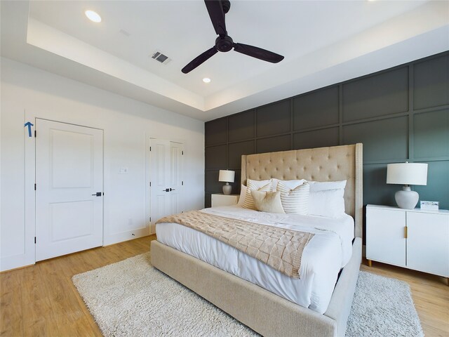 bedroom with a raised ceiling, ceiling fan, and light hardwood / wood-style flooring