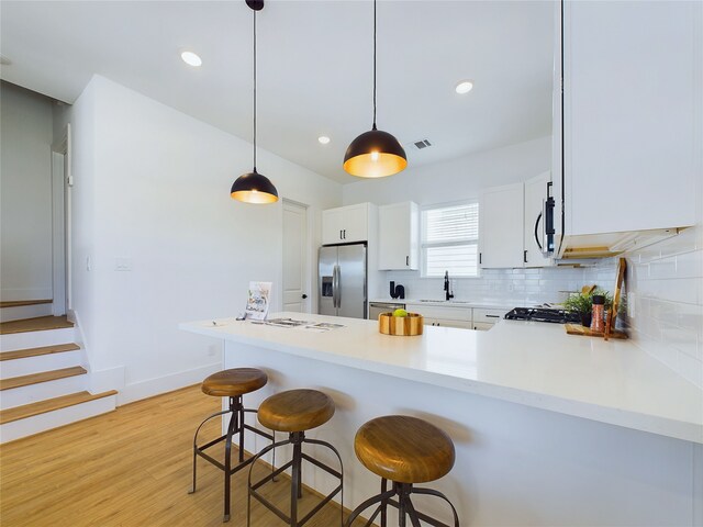 kitchen featuring white cabinets, light hardwood / wood-style flooring, decorative light fixtures, kitchen peninsula, and stainless steel appliances