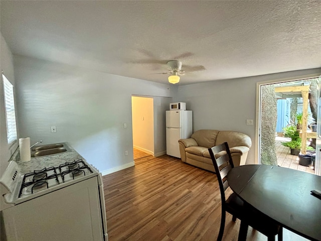 kitchen featuring white appliances, sink, ceiling fan, light wood-type flooring, and a textured ceiling