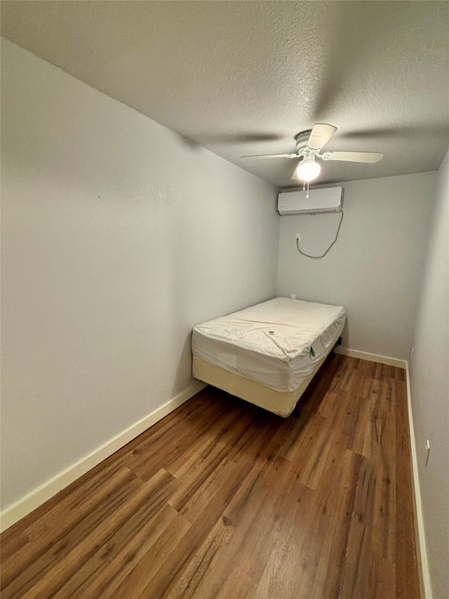 unfurnished bedroom with hardwood / wood-style flooring, ceiling fan, an AC wall unit, and a textured ceiling