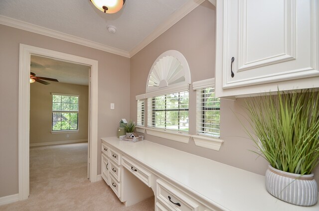 carpeted office featuring ceiling fan, built in desk, ornamental molding, and a wealth of natural light