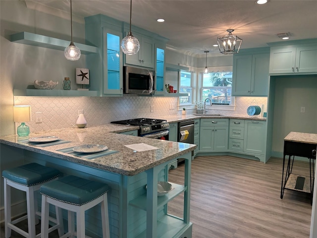 kitchen with sink, light stone counters, appliances with stainless steel finishes, kitchen peninsula, and pendant lighting