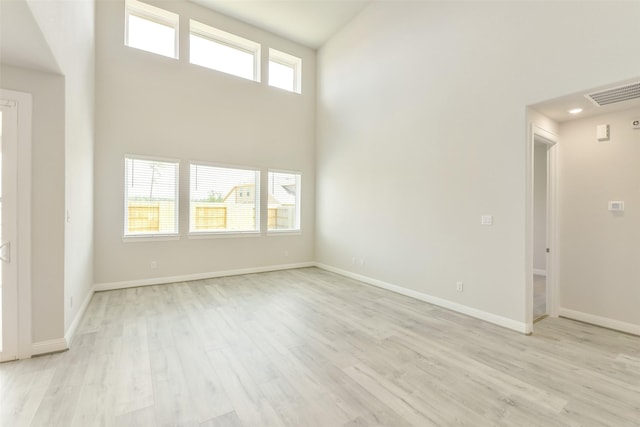 unfurnished living room with light wood finished floors, baseboards, visible vents, and a high ceiling