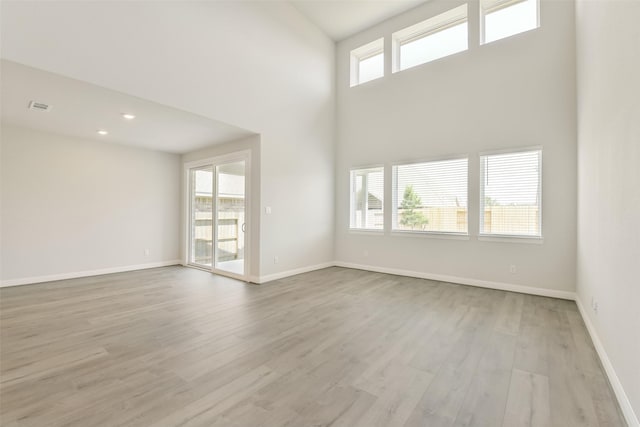 unfurnished living room featuring a towering ceiling, light wood-style flooring, visible vents, and baseboards