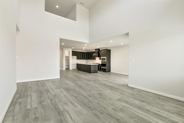 unfurnished living room with recessed lighting, light wood-type flooring, a high ceiling, and baseboards