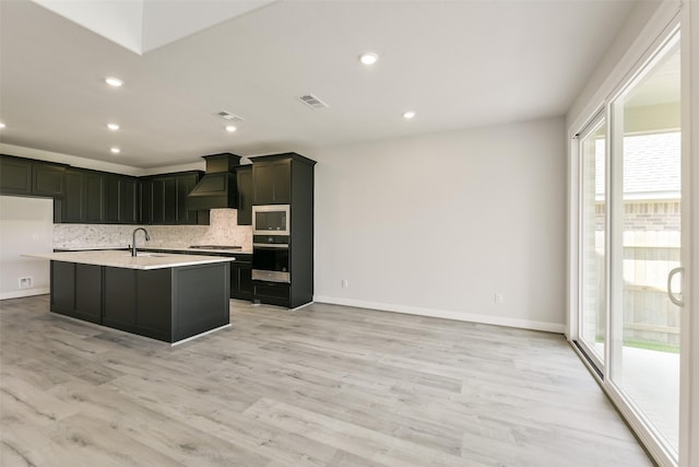 kitchen with tasteful backsplash, a sink, light countertops, premium range hood, and appliances with stainless steel finishes