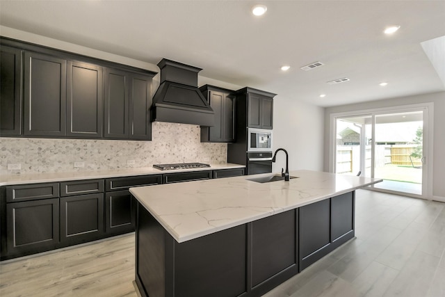 kitchen featuring a sink, built in microwave, visible vents, decorative backsplash, and custom range hood
