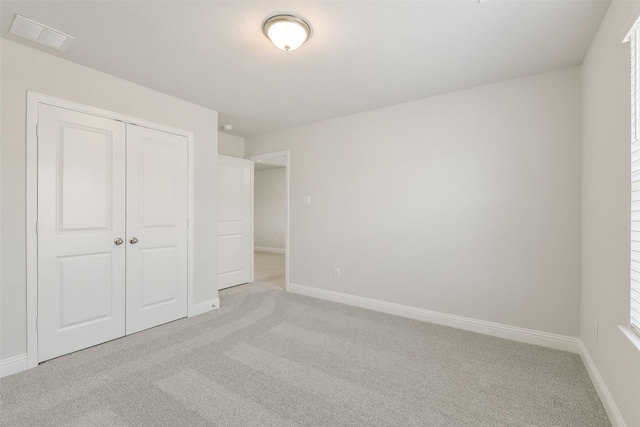 unfurnished bedroom featuring light colored carpet, baseboards, visible vents, and a closet