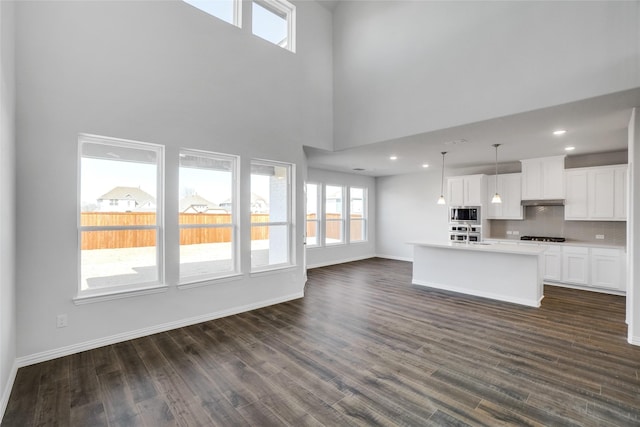 kitchen with dark hardwood / wood-style floors, white cabinetry, an island with sink, and hanging light fixtures