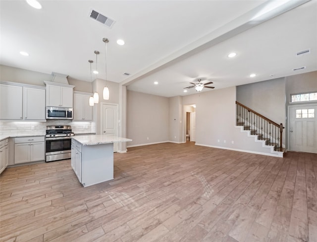 kitchen with white cabinets, a center island, light wood-type flooring, and appliances with stainless steel finishes