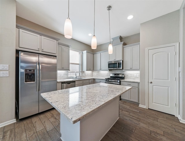 kitchen featuring a center island, light stone counters, dark hardwood / wood-style flooring, pendant lighting, and appliances with stainless steel finishes