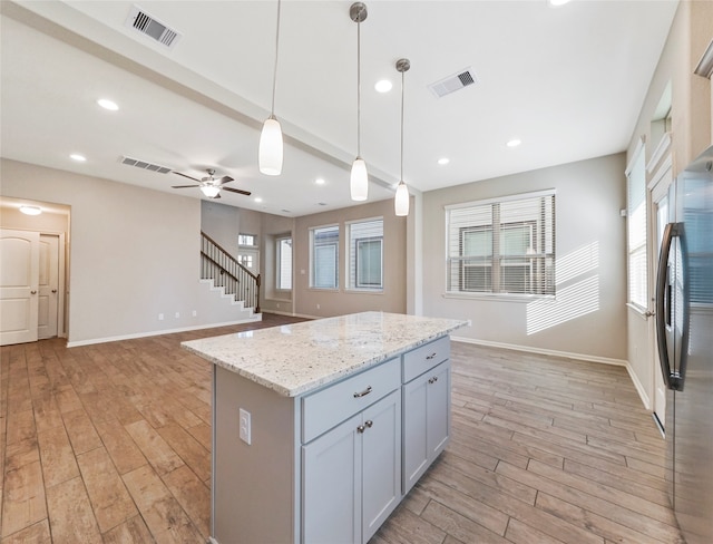 kitchen with stainless steel refrigerator, a center island, decorative light fixtures, and light wood-type flooring