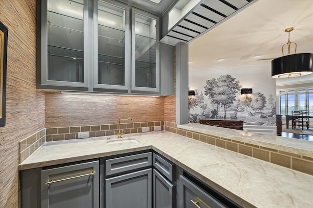 bar featuring light stone countertops, sink, decorative light fixtures, gray cabinets, and decorative backsplash