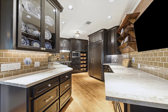 kitchen with light wood-type flooring, tasteful backsplash, built in appliances, and dark brown cabinetry