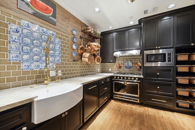 kitchen with sink, light stone counters, light hardwood / wood-style flooring, decorative backsplash, and appliances with stainless steel finishes