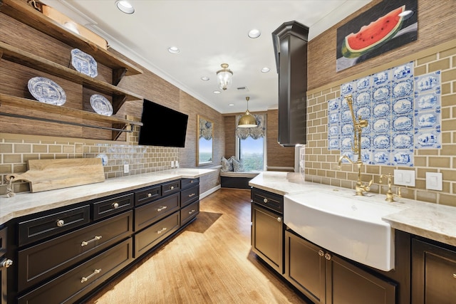 kitchen with decorative light fixtures, light hardwood / wood-style floors, decorative backsplash, and crown molding