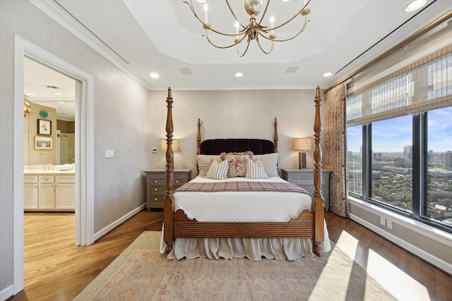 bedroom featuring ornamental molding, a raised ceiling, an inviting chandelier, hardwood / wood-style floors, and connected bathroom