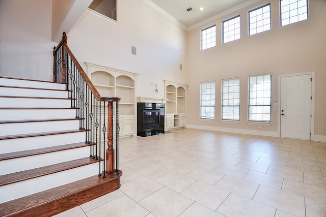 unfurnished living room featuring built in features, crown molding, light tile patterned floors, and a towering ceiling