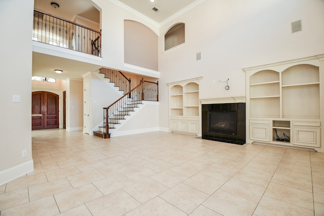 unfurnished living room with a high ceiling, crown molding, light tile patterned floors, built in features, and a fireplace