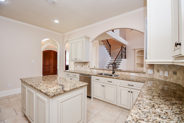 kitchen with decorative backsplash, light stone counters, sink, dishwasher, and a kitchen island