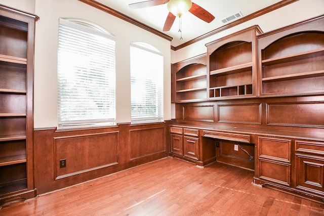 unfurnished office featuring ceiling fan, light hardwood / wood-style floors, built in desk, and ornamental molding