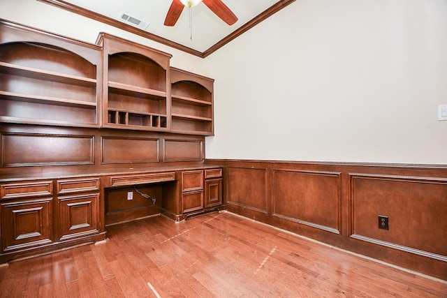 unfurnished office with ceiling fan, wood-type flooring, built in desk, and crown molding