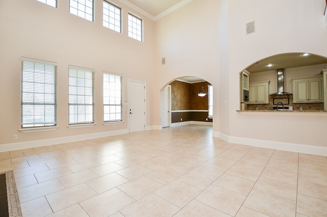 unfurnished living room featuring light tile patterned floors, a towering ceiling, crown molding, and a healthy amount of sunlight