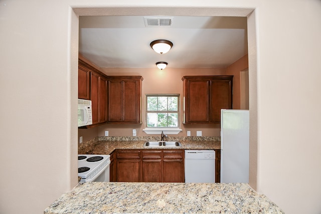 kitchen with white appliances, light stone counters, and sink