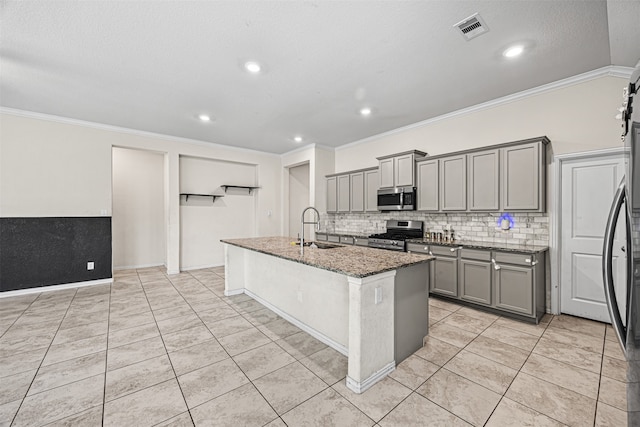 kitchen featuring appliances with stainless steel finishes, a kitchen island with sink, sink, dark stone countertops, and gray cabinets