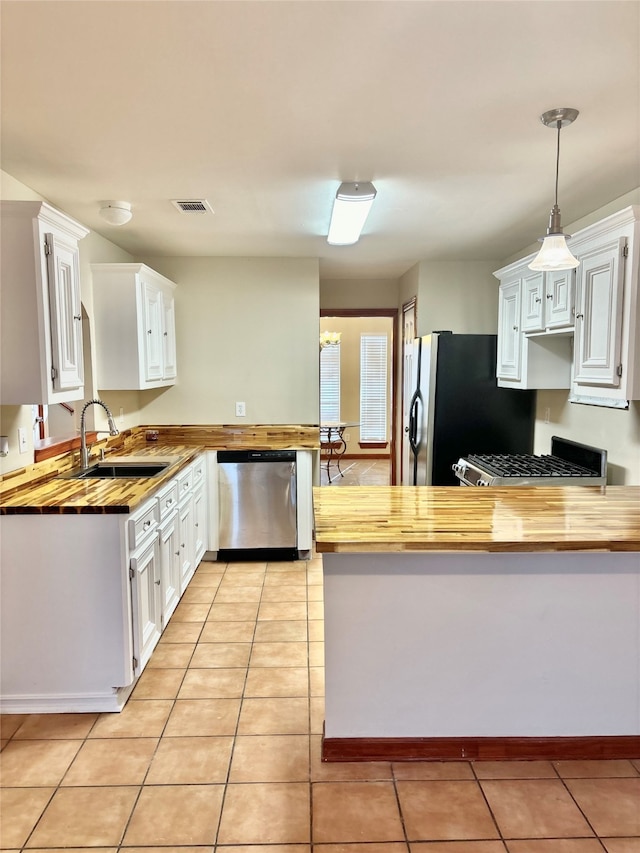 kitchen featuring butcher block countertops, white cabinetry, hanging light fixtures, and appliances with stainless steel finishes