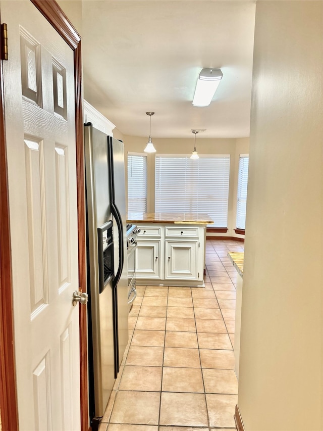 kitchen with kitchen peninsula, appliances with stainless steel finishes, light tile patterned floors, white cabinetry, and hanging light fixtures