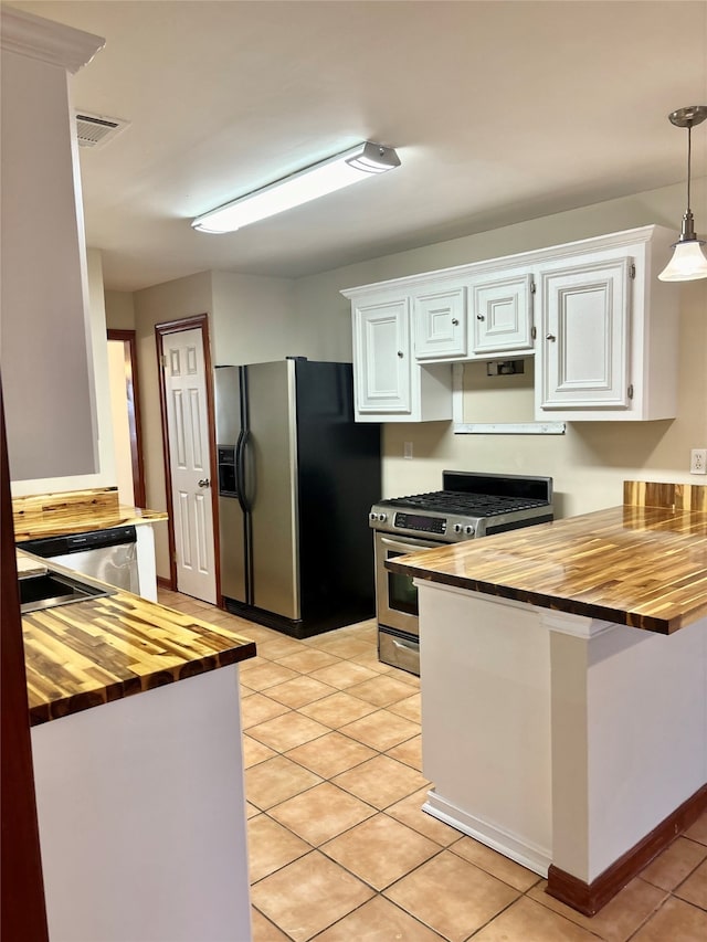 kitchen with wood counters, appliances with stainless steel finishes, pendant lighting, light tile patterned floors, and white cabinetry