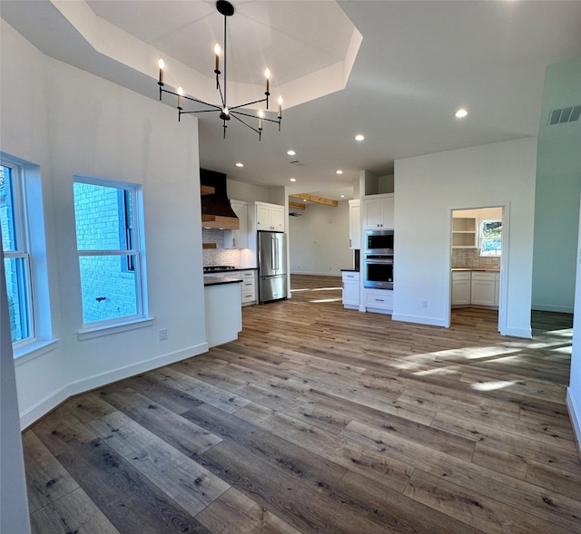 unfurnished living room with a tray ceiling, a chandelier, and wood-type flooring