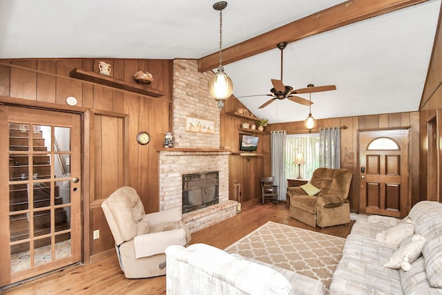 living room featuring vaulted ceiling with beams, wood walls, light hardwood / wood-style flooring, and a fireplace